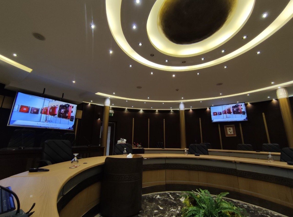 Curved boardroom table with built-in microphones, facing a wall-mounted display mirroring a presentation