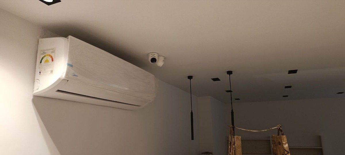 CCTV dome camera mounted on the ceiling above a wall-mounted air conditioning unit