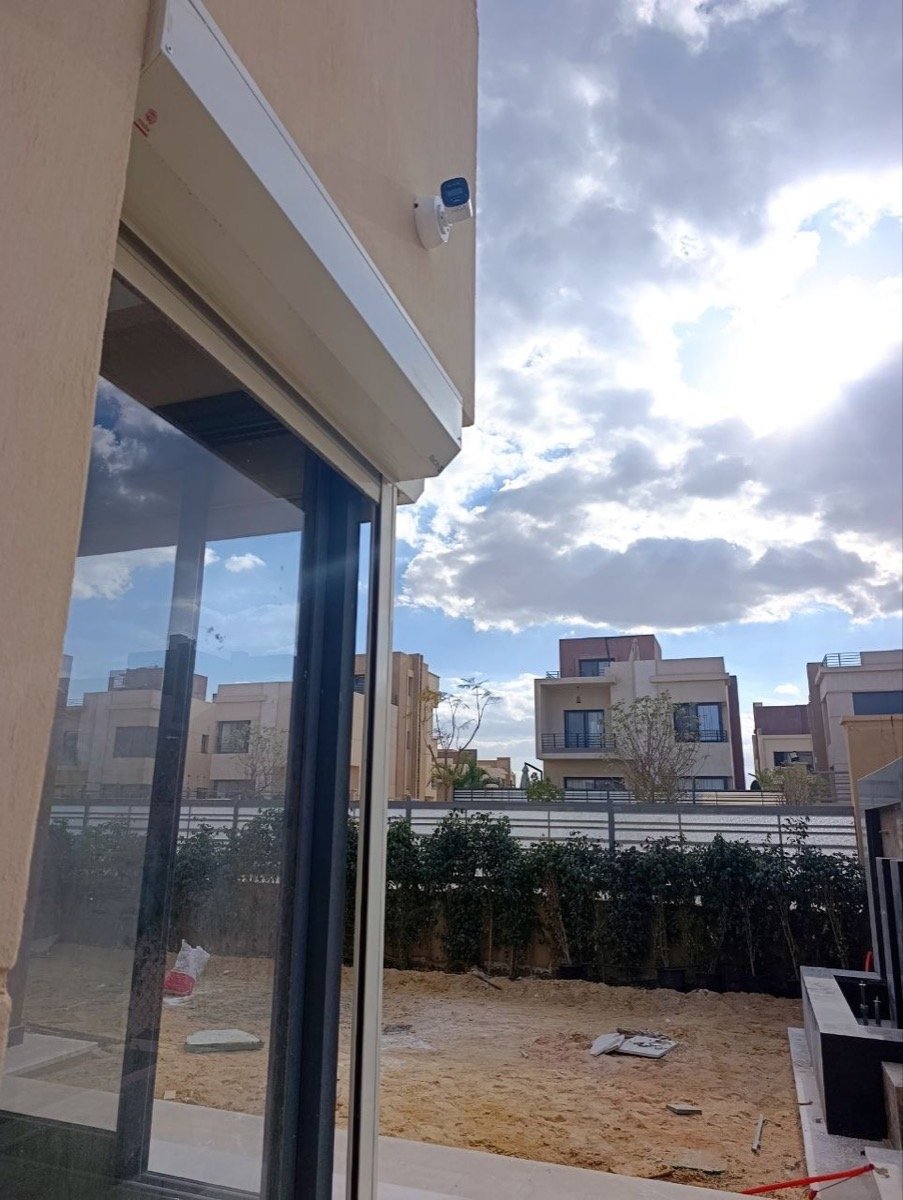 CCTV camera mounted above a glass sliding door, overlooking the back terrace under construction