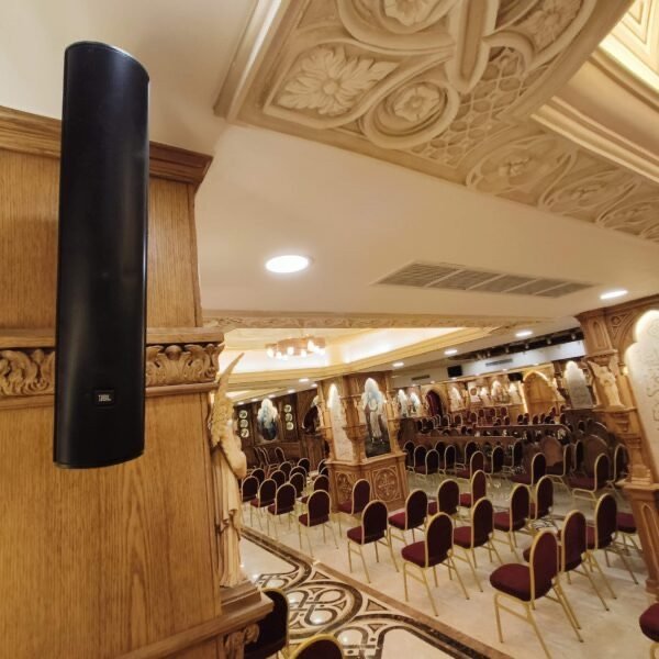 Ceiling-height speaker mounted on an ornate column, overlooking rows of seating in the hall