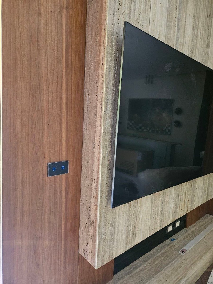 Smart touch switch beside a wall-mounted TV on a travertine-clad media wall