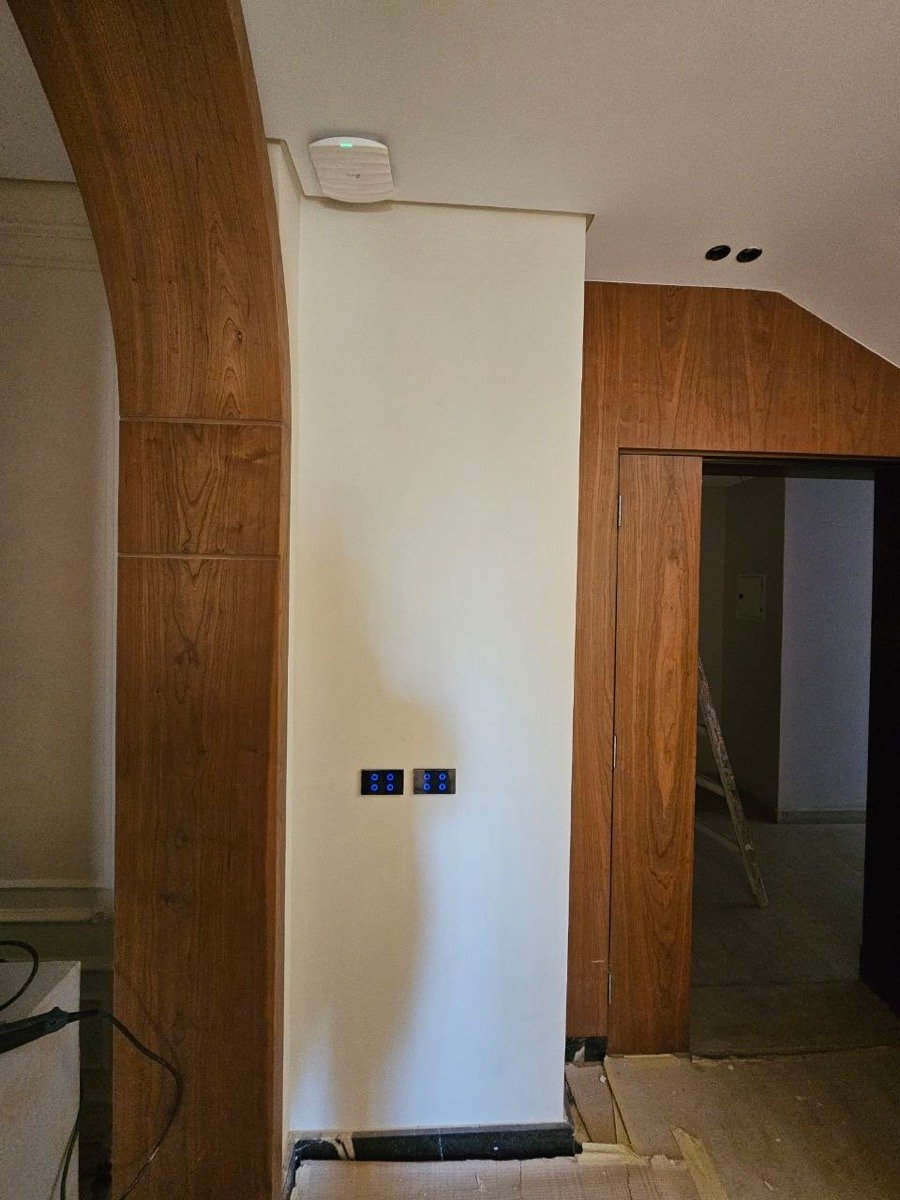 Ceiling-mounted wireless access point above smart touch switch panels in a corridor, during construction