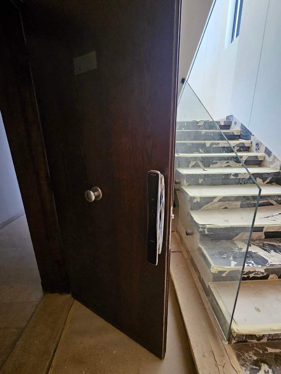 Fingerprint smart door lock installed on a wooden entry door overlooking a glass-railed staircase